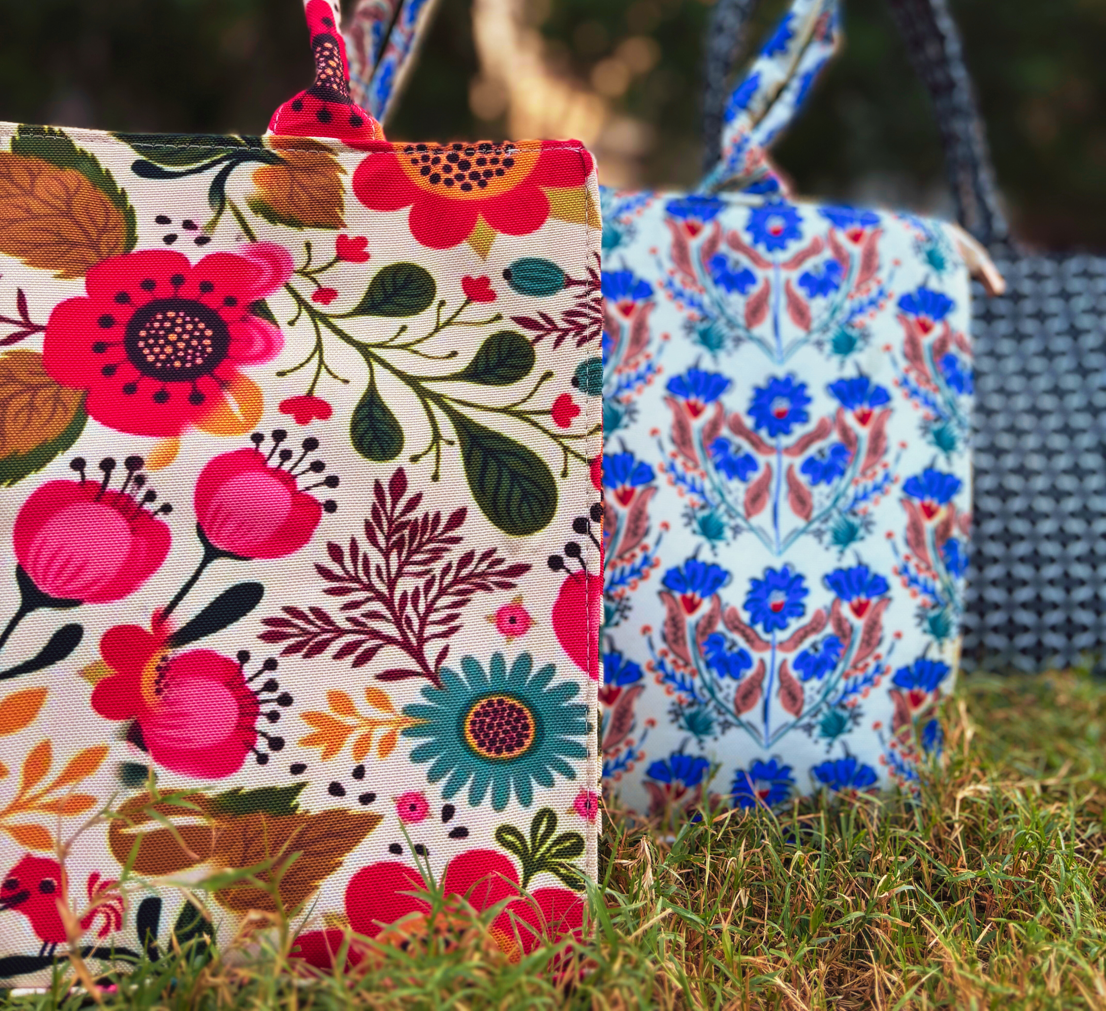 Three colorful canvas tote bags with floral patterns displayed on green grass.